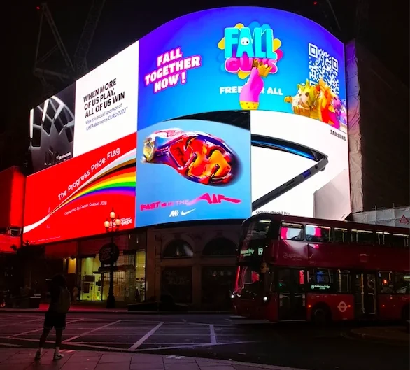 Vista nocturna de Piccadilly Circus, con pantallas electrónicas brillantes y un autobús rojo de dos pisos en primer plano.