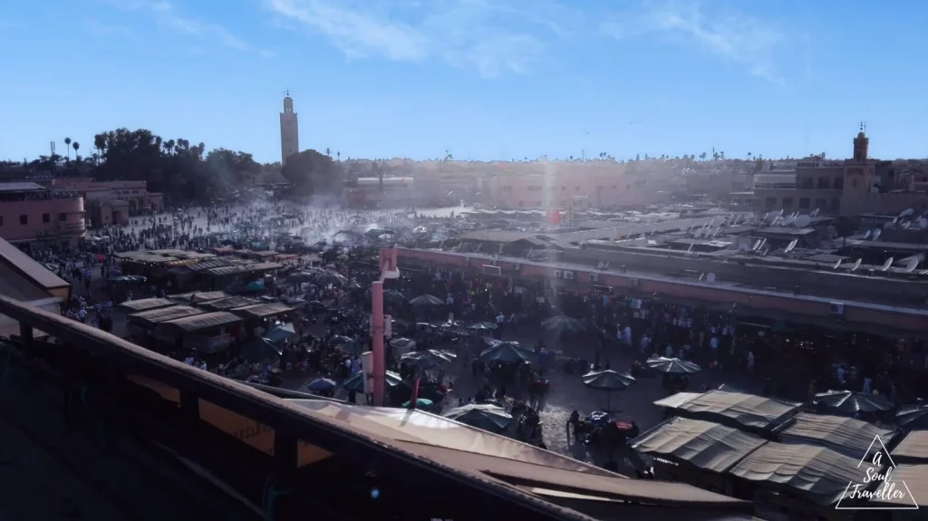Vista panorámica de la plaza Jemaa el-Fnaa en Marrakech, Marruecos, con puestos de mercado tradicionales, multitudes de personas y el minarete de la mezquita Koutoubia al fondo bajo un cielo azul. Destino donde viajar en enero