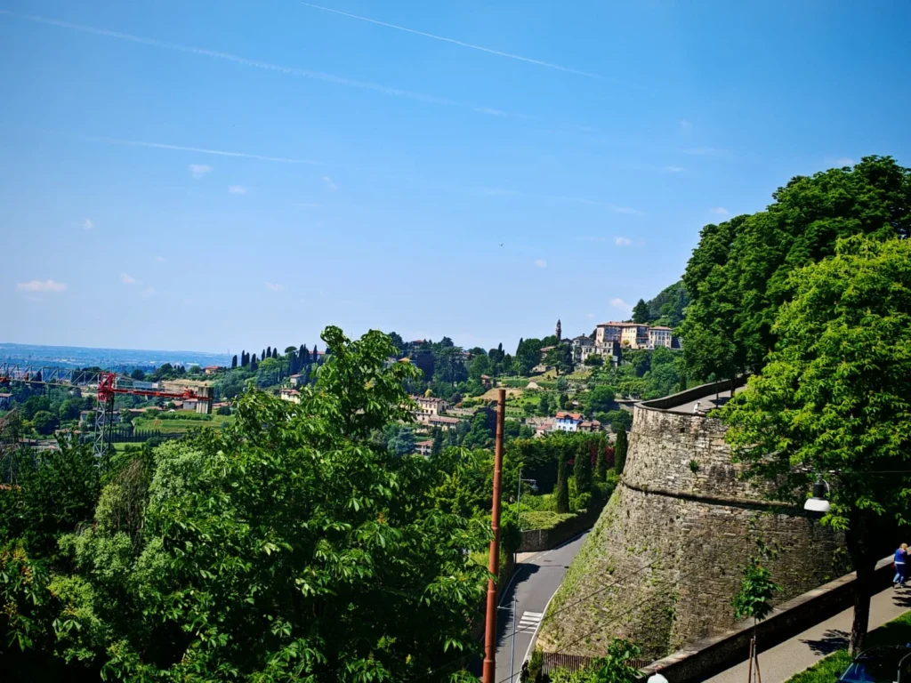 Mura Venete de Bérgamo con Porta San Giacomo y paisaje verde, con colinas y casas históricas al fondo. Imprescincible que ver en Bérgamo en 1 día