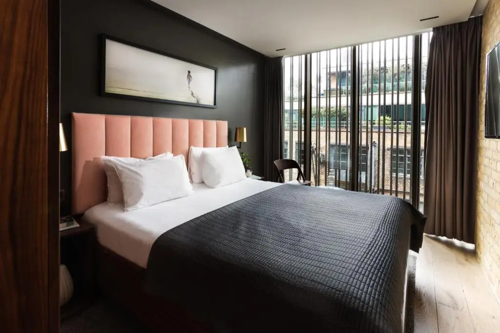 Habitación de hotel boutique en Londres con cama doble, cabecero rosa y gran ventanal; ejemplo de alojamiento céntrico para parejas — mejores zonas para alojarse en Londres.