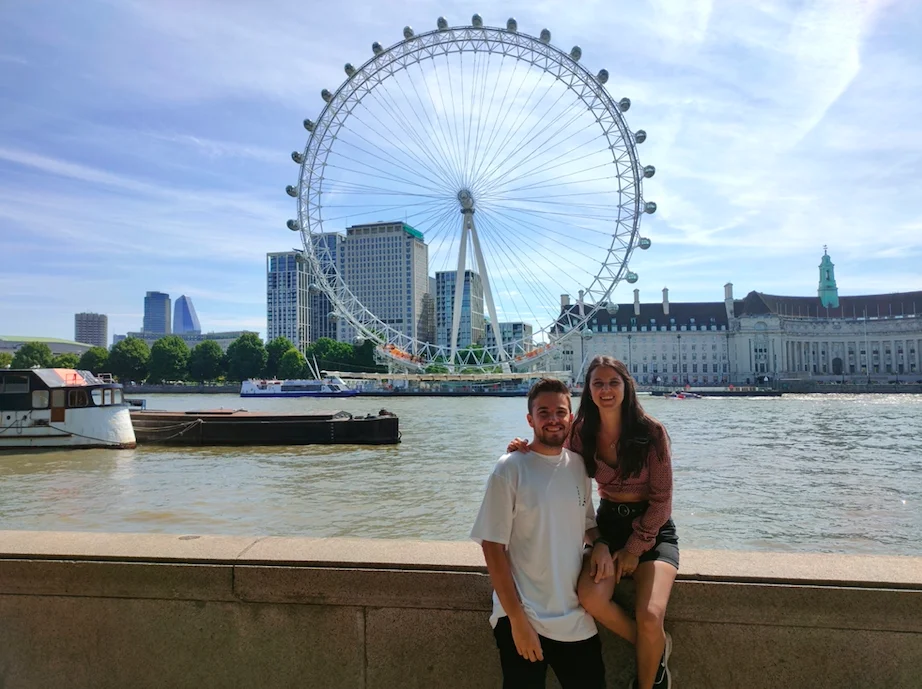 Pareja posando frente al London Eye, con el río Támesis y el skyline de Londres al fondo, en un día soleado