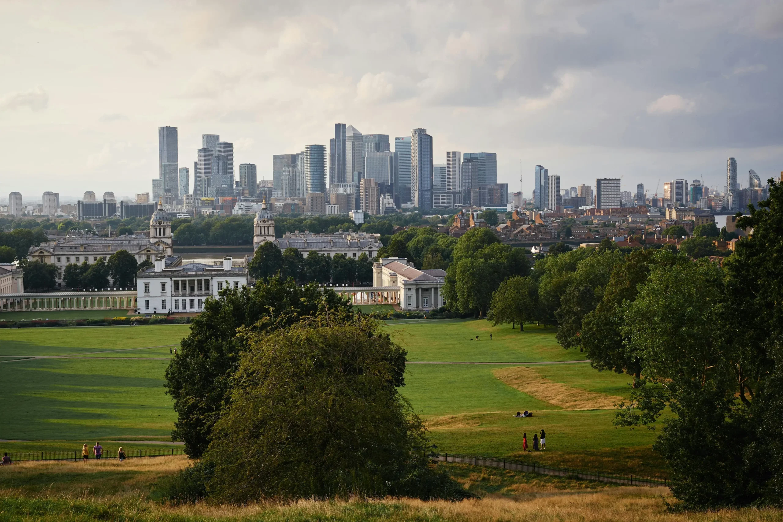 Vista panorámica desde Greenwich Park, mostrando el horizonte de la ciudad de Londres con rascacielos modernos y el histórico Old Royal Naval College en primer plano