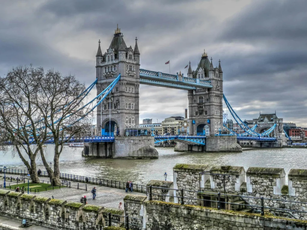 Vista del Tower Bridge en Londres desde el río Támesis, con el puente elevado parcialmente y el cielo nublado al fondo