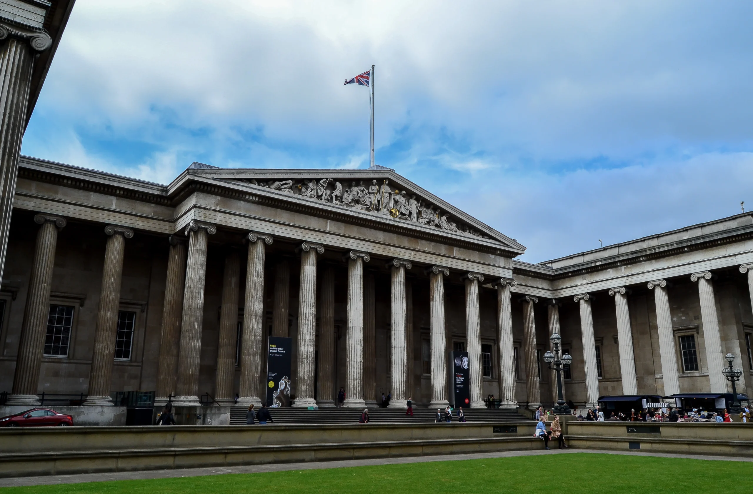 Fachada del Museo Británico en Londres, con su imponente arquitectura de columnas clásicas y un cielo parcialmente nublado en el fondo