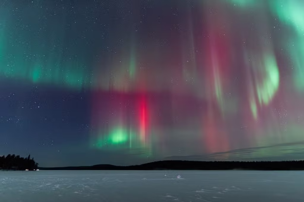 Auroras boreales de colores verde y rosa iluminando el cielo nocturno estrellado sobre un paisaje nevado y un lago congelado en Rovaniemi, Laponia finlandesa.