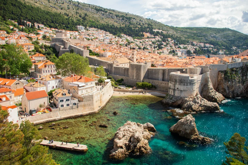 Vista aérea panorámica de la ciudad vieja de Dubrovnik, Croacia, mostrando sus icónicos tejados de terracota roja, las antiguas murallas de piedra frente al mar Adriático azul profundo y el puerto deportivo. Un destino perfecto para viajar en mayo